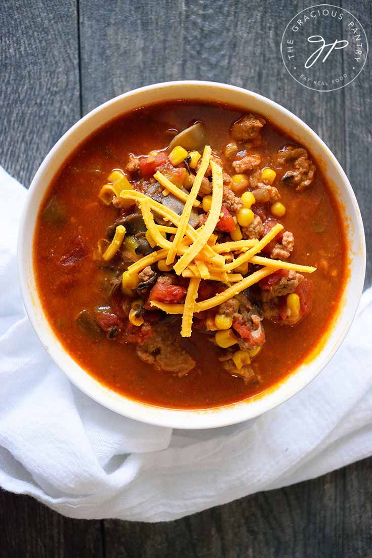 And overhead view of this Instant Pot Turkey Chili in a white bowl. You can see bits of turkey and corn and tomatoes with shredded cheddar sprinkled over the top.