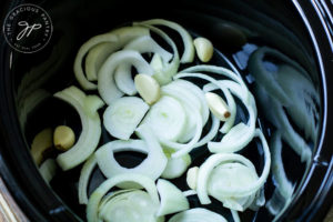 Step one of this Slow Cooker Pork Loin Recipe shows the onions and garlic cloves in the base of the slow cooker insert.