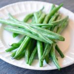 A single, white plate sits piled high with bright green, Air Fryer Green Beans.