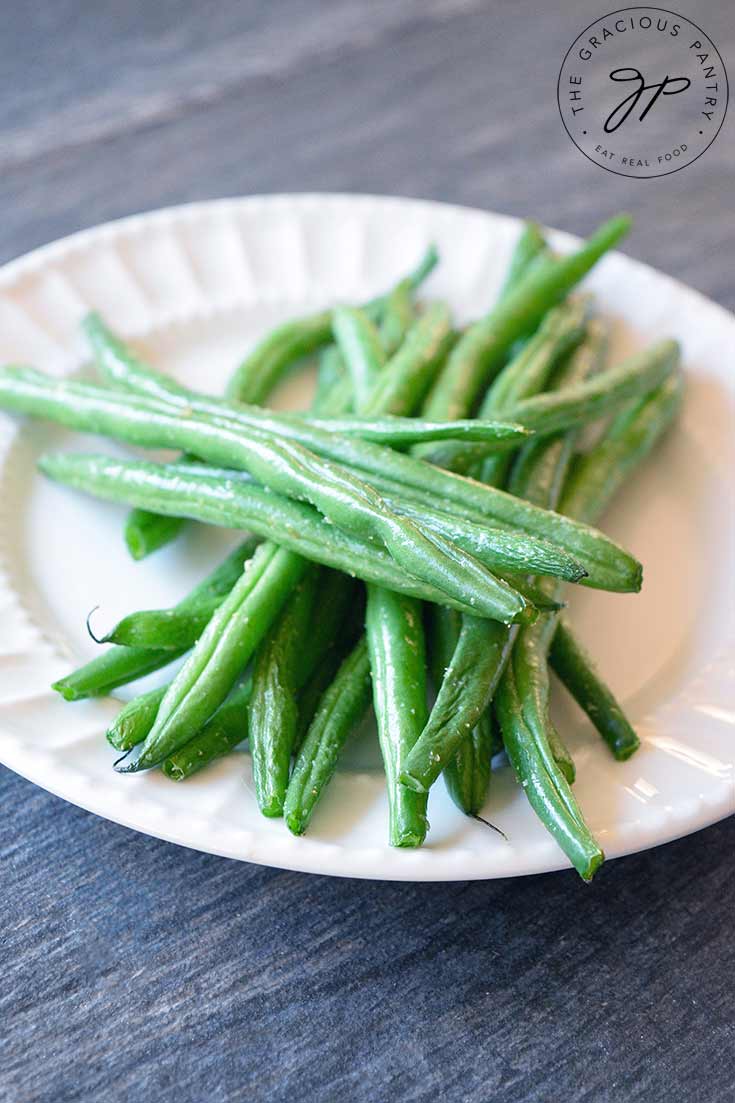 A single, white plate sits piled high with bright green, Air Fryer Green Beans.