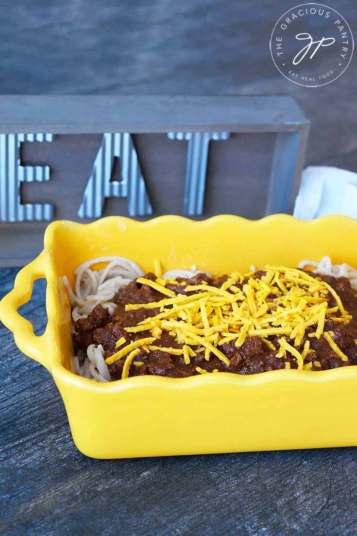 A yellow casserole dish filled with Cincinnati chili covered pasta, sits next to a wooden sign that says, "eat".