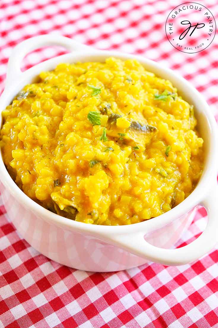 A white bowl of this Butternut Squash Risotto sits ready to eat on a white and red checkered tablecloth.