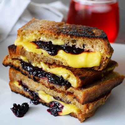 A Grilled Cheese Sandwich With Blackberries sits with a glass of juice behind it, ready to enjoy for lunch.