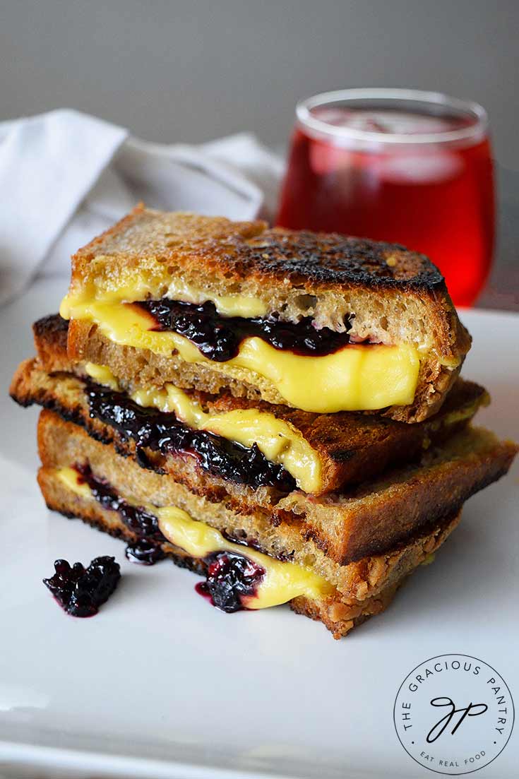 A Grilled Cheese Sandwich With Blackberries sits with a glass of juice behind it, ready to enjoy for lunch.