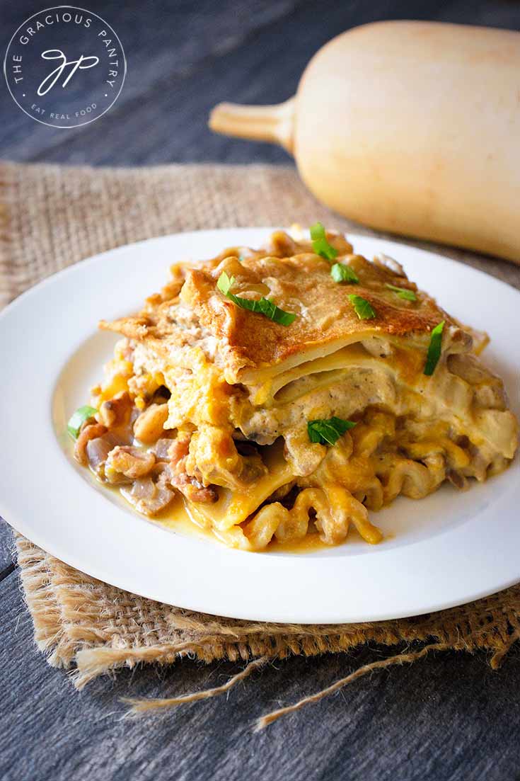 A white plate sits on a piece of burlap with a slice of this Butternut Squash Lasagna sitting on it, ready to serve.