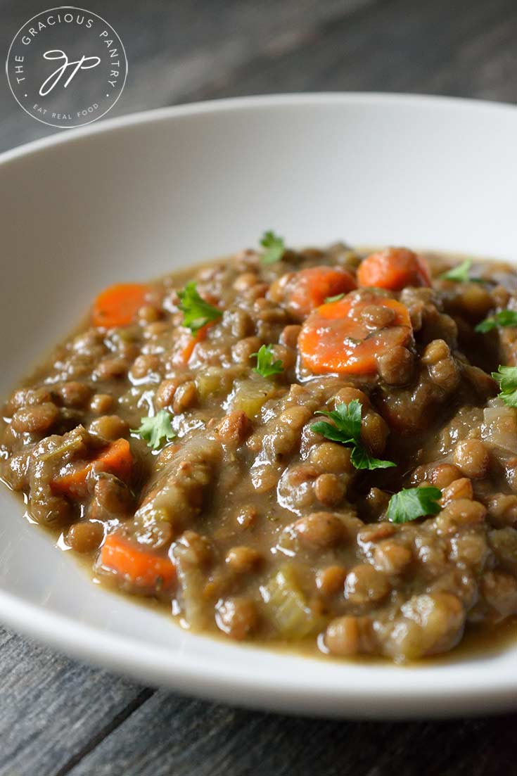 A white bowl sits on a table with a nice helping of this Vegan Instant Pot Lentil Soup. You can see carrot slices in with the lentils and fresh herbs sprinkled over the top.