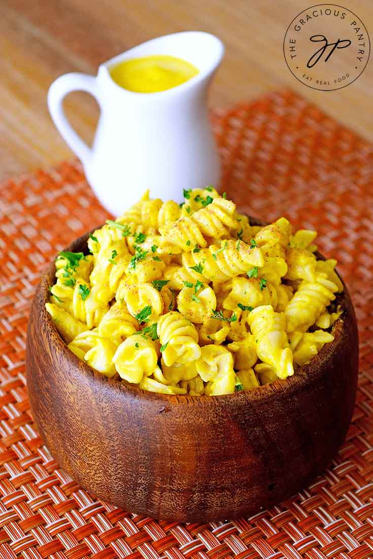 A wooden bowl, filled with pasta, sits on a table with a small pitcher of Butternut Squash Pasta Sauce sitting behind it.