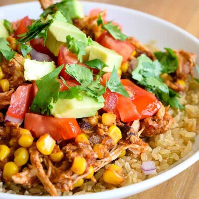 An up close shot of this Instant Pot Mexican Chicken shows the chicken on brown rice with fresh tomatoes, avocado and cilantro sprinkled over the top.