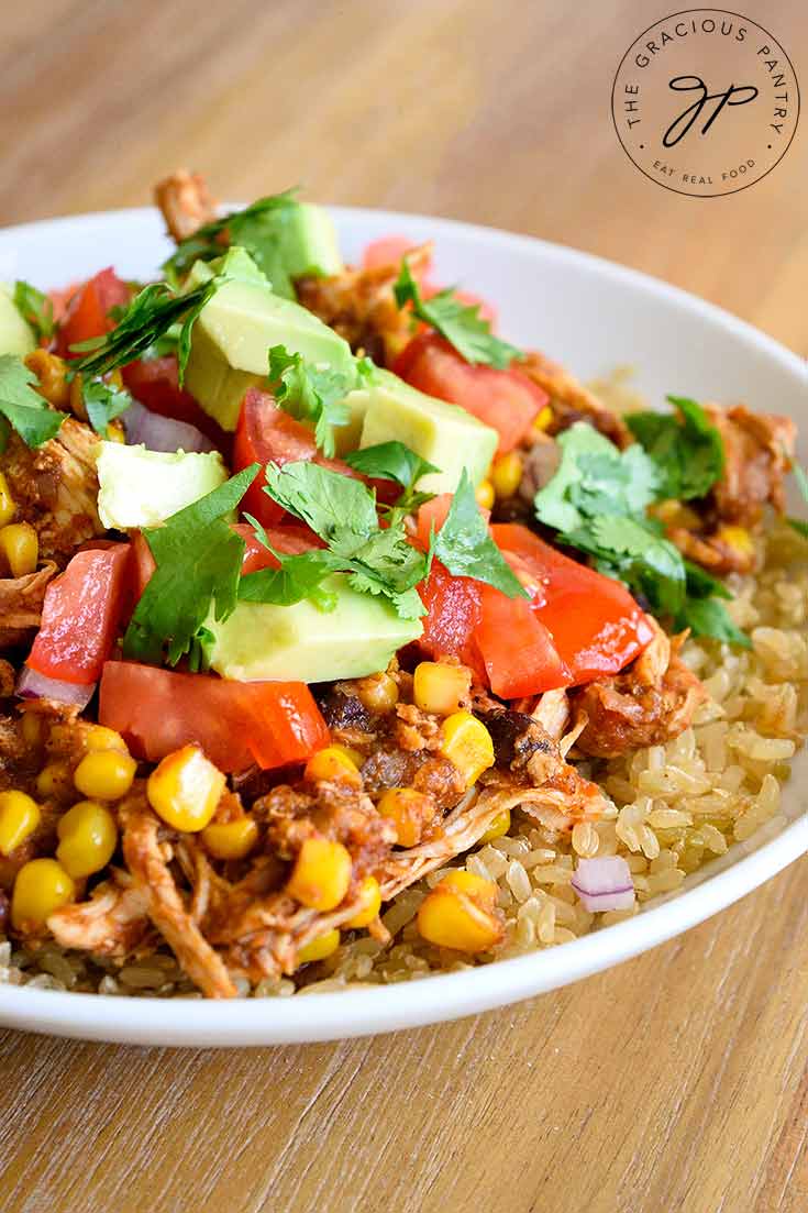 An up close shot of this Instant Pot Mexican Chicken shows the chicken on brown rice with fresh tomatoes, avocado and cilantro sprinkled over the top.