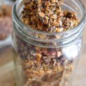 A canning jar sits filled with this Pumpkin Spice Granola Bark. The lid is off so you can see the bark inside the jar from the top as well as the sides.