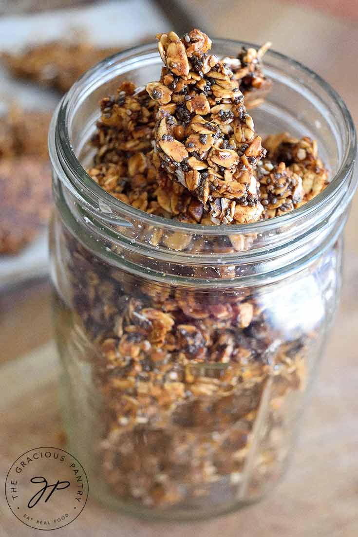 A canning jar sits filled with this Pumpkin Spice Granola Bark. The lid is off so you can see the bark inside the jar from the top as well as the sides.