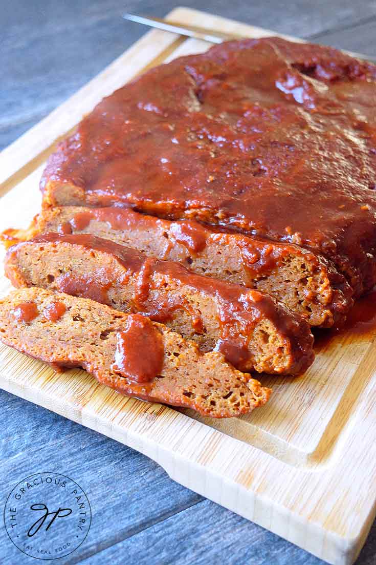 A Seitan Brisket With Barbecue Glaze sits partially sliced on a cutting board with barbecue sauce drizzled over the top of the brisket.