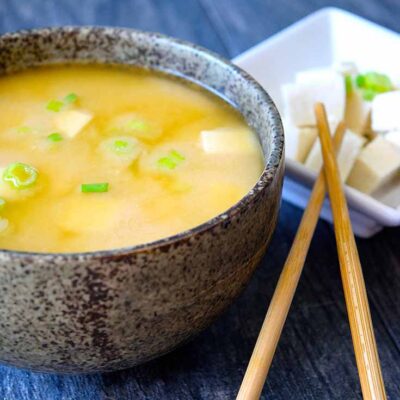 A delicious bowl of miso soup sits next to a smaller bowl of tofu with sliced green onions on top.