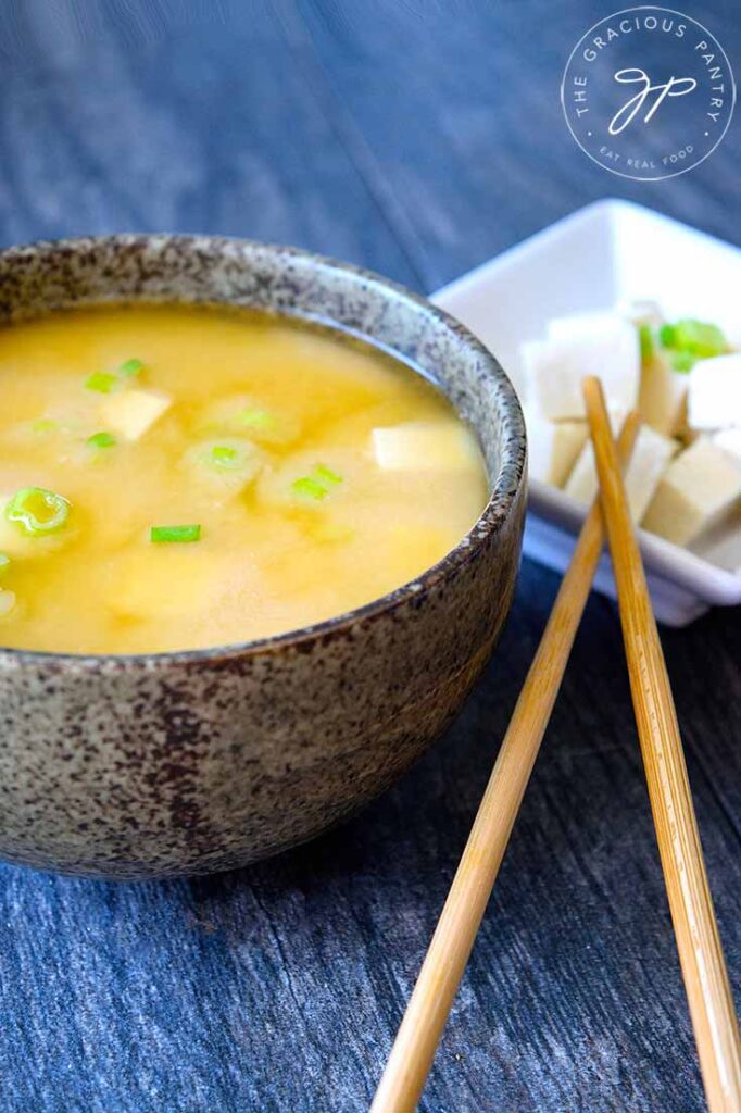 A delicious bowl of miso soup sits next to a smaller bowl of tofu with sliced green onions on top.