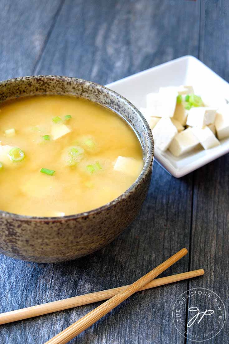 An overhead view of this miso soup recipe. The soup is in a gray bowl and you can see bits of tofu and green onion floating in the golden brown broth.