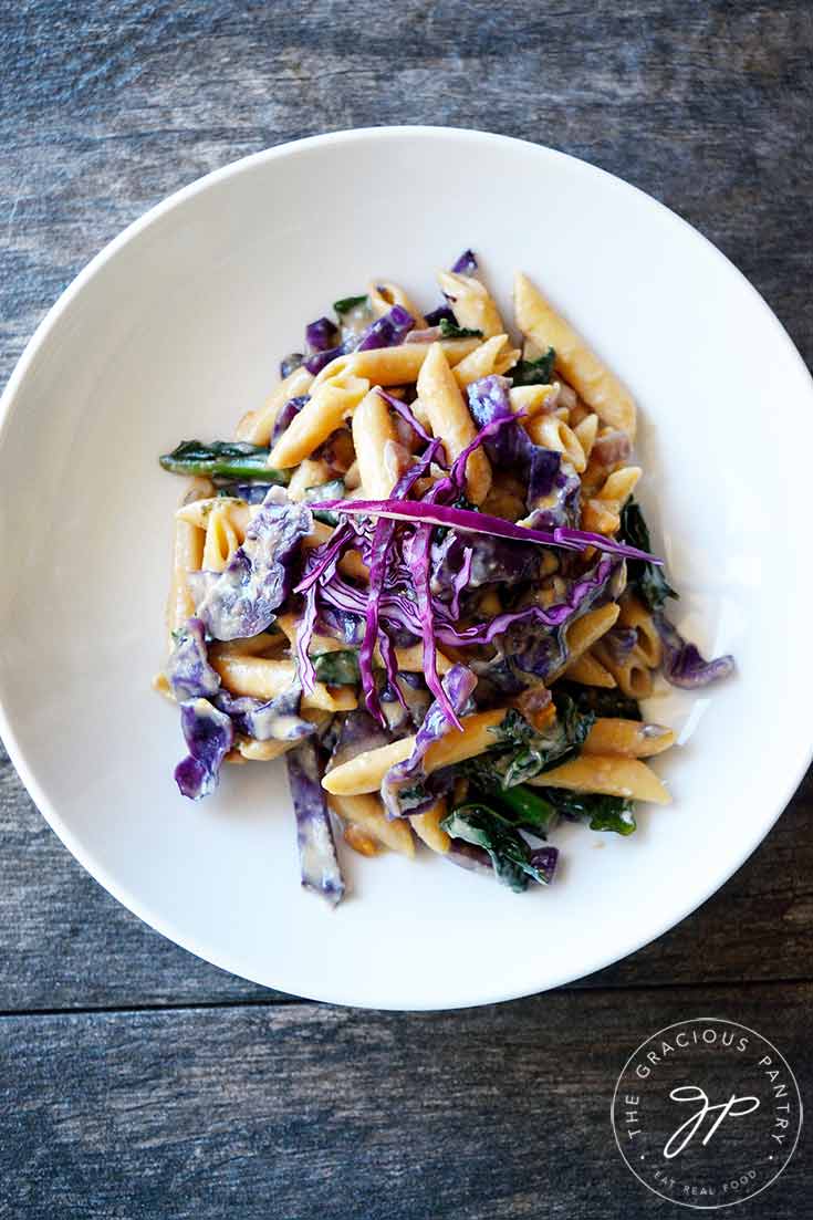 This Red Cabbage Pasta sits in a white bowl and the view is from overhead. You can see lots of red cabbage and bits of green kale mixed into the noodles.