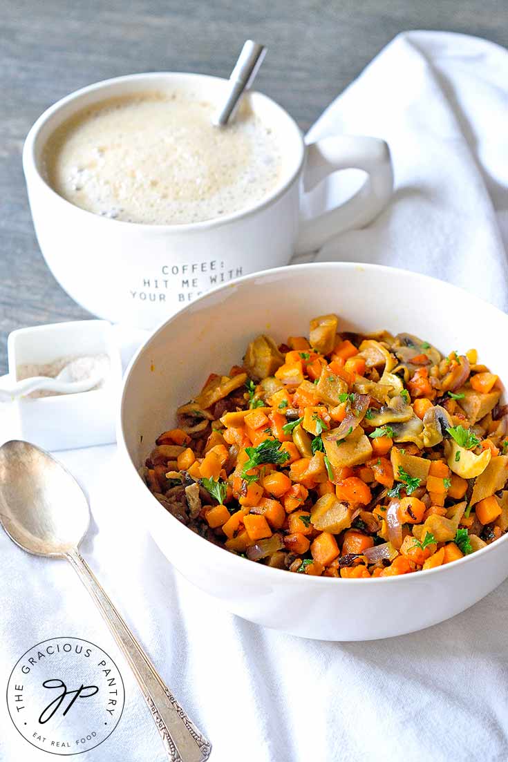 This Sweet Potato Breakfast Scramble With Seitan, sits in a white bowl, ready to eat. A cup of coffee sits next to it.