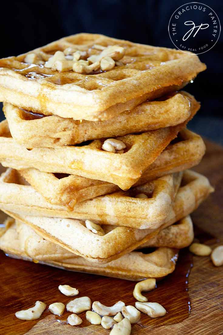 A close up shot of this big stack of Vegan Waffles sits on a wooden cutting board. The maple syrup is dripping down the sides of the stack.