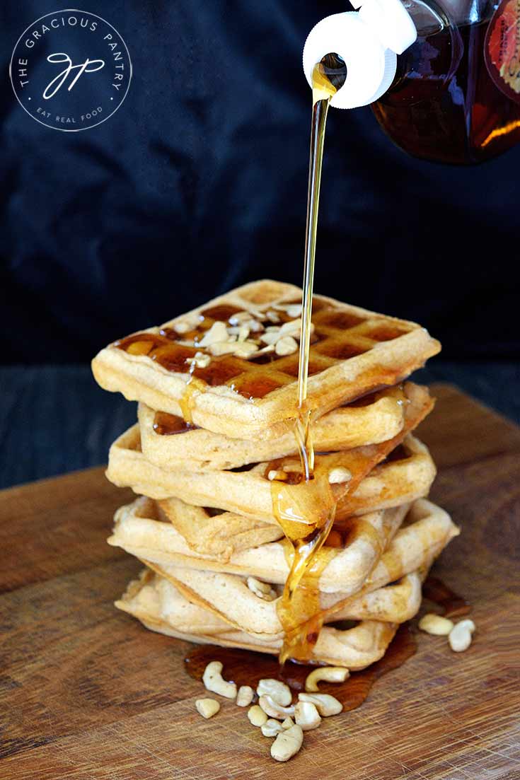A stack of waffles made from this Vegan Waffles Recipe, are having maple syrup poured over the top. It's drizzling down the side into an amber pool of syrup at the bottom.