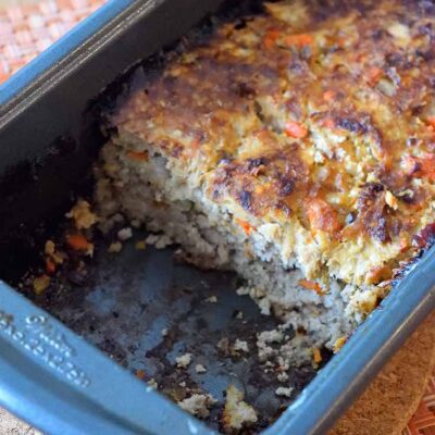 The cooked ground turkey meatloaf sits partially cut in the loaf pan. A piece of the meatloaf has been removed.