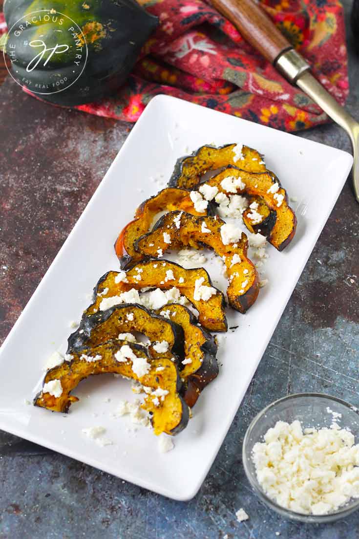 A platter of this Roasted Acorn Squash With Feta sits on a table with a bowl of feta crumbles next to it, all ready to serve.