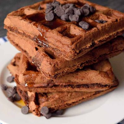 An up close side view of this large stack of waffles. Maple syrup drips down the side.