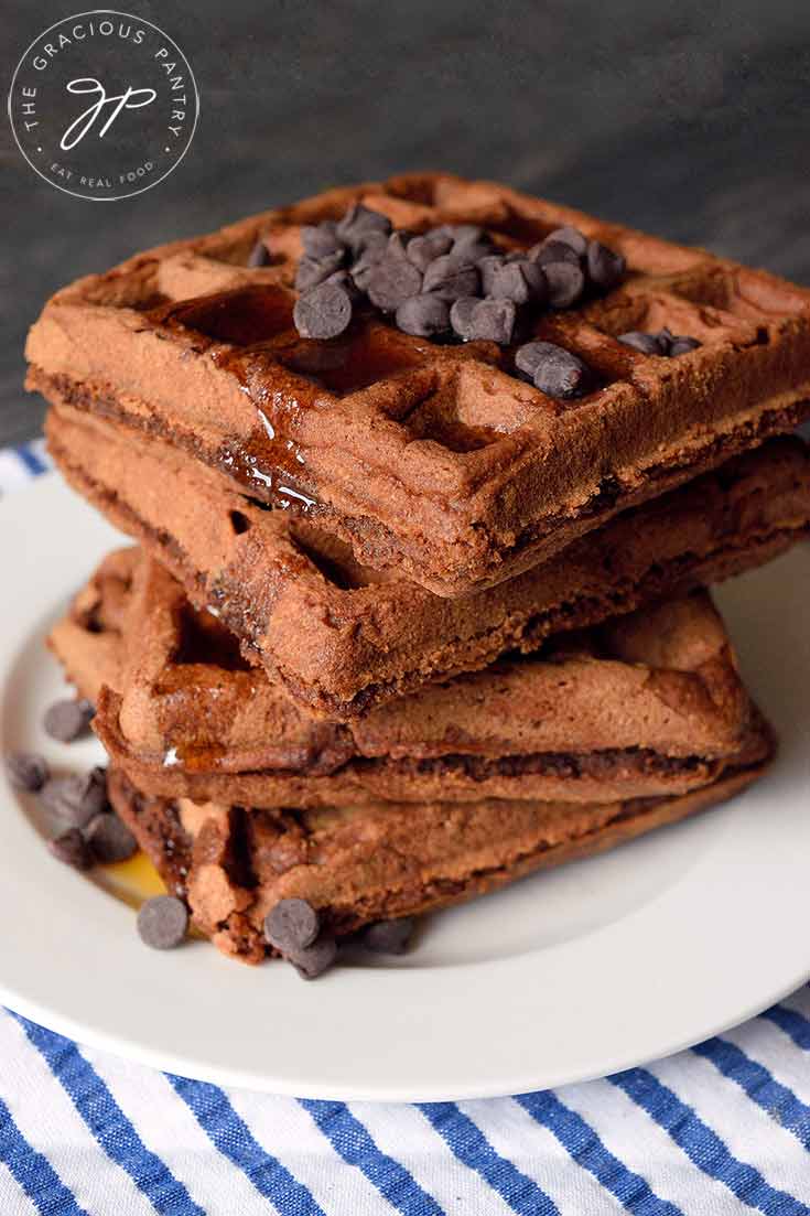 An up close side view of this large stack of waffles. Maple syrup drips down the side.