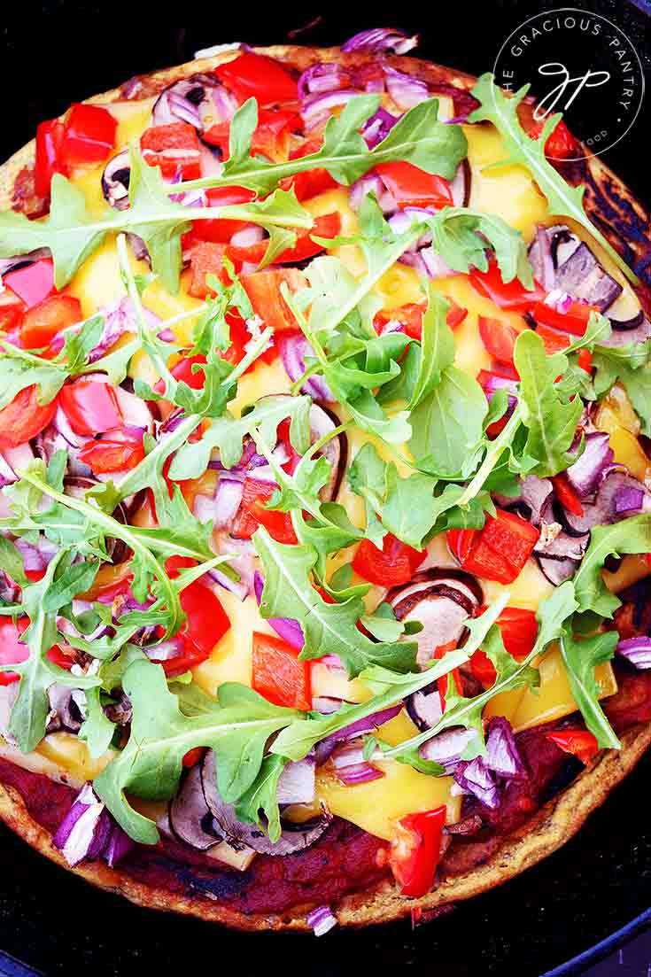 An overhead view of this Vegan Pizza Dough with all it's toppings. You can see arugula, red peppers, purple onions and the creamy yellow of the vegan cheese.