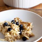Baked Oatmeal Recipe served at the table in white dishes. Fresh blueberries garnish the oatmeal.