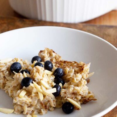 Baked Oatmeal Recipe served at the table in white dishes. Fresh blueberries garnish the oatmeal.