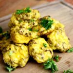 A batch of freshly baked Mini Egg Muffins sit on a cutting board sprinkled with fresh parsley.