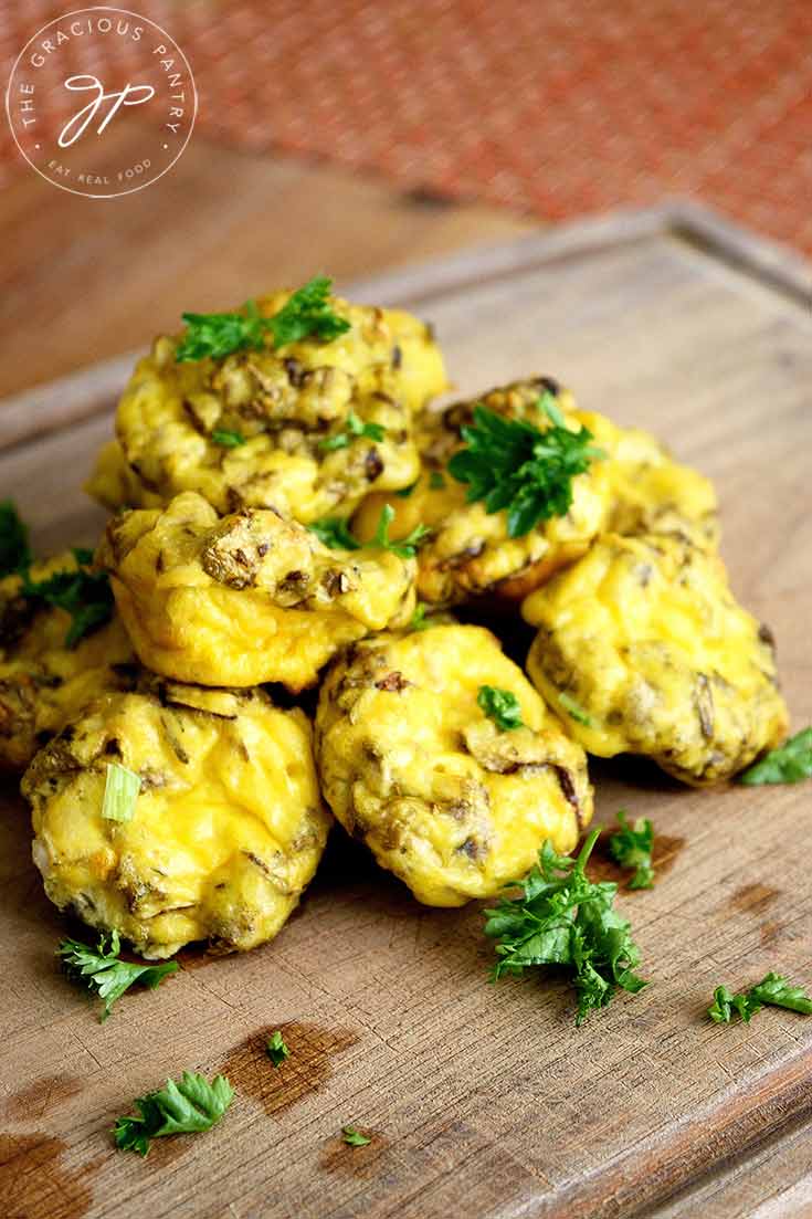 A batch of freshly baked Mini Egg Muffins sit on a cutting board sprinkled with fresh parsley.