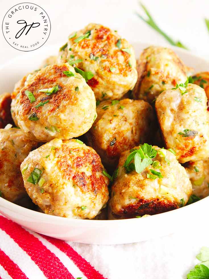 A white bowl filled with ground turkey meatballs sits on a white table, ready to serve.