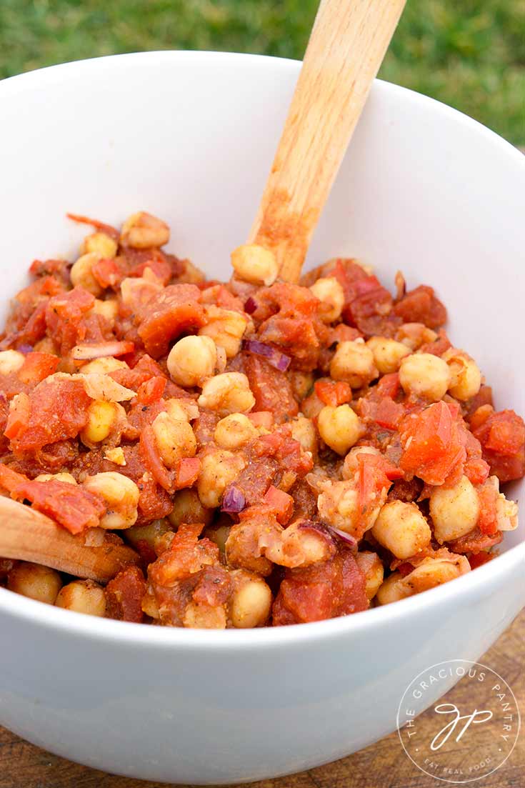 A white serving bowl with a wooden spoon sits filled with this Indian Chickpea Salad, ready to serve.