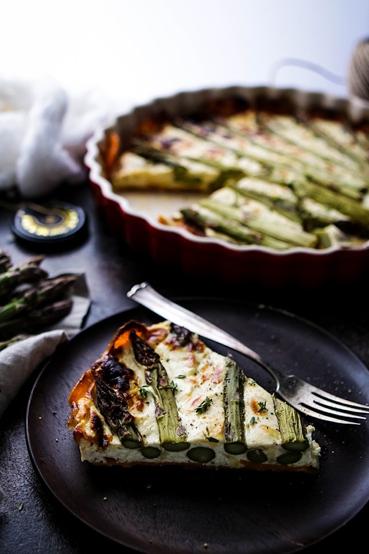 A single slice of Asparagus Quiche on a black plate with a fork resting next to it.