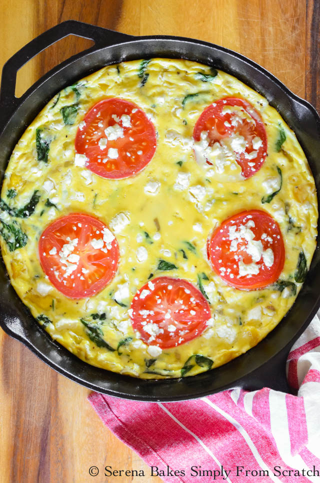 A frittata in a cast iron pan on a table, with slices of tomato on top.