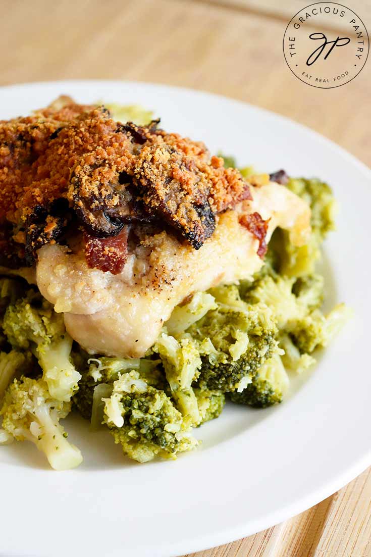 A Bacon Stuffed Chicken Thigh sits on a base of broccoli on a white plate. Just one idea for serving this deliciousness.