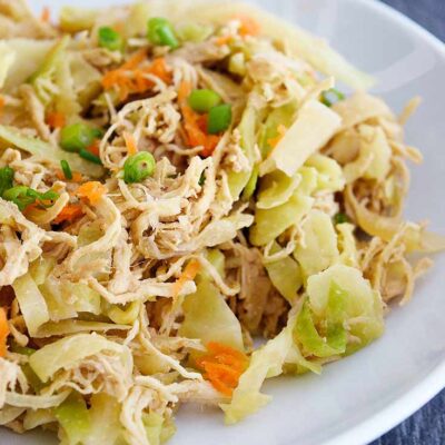 A white bowl filled with this Egg Roll In A Bowl Recipe sits on a slate tabletop. You can see bits of chicken, cabbage, shredded carrots and sliced green onions.