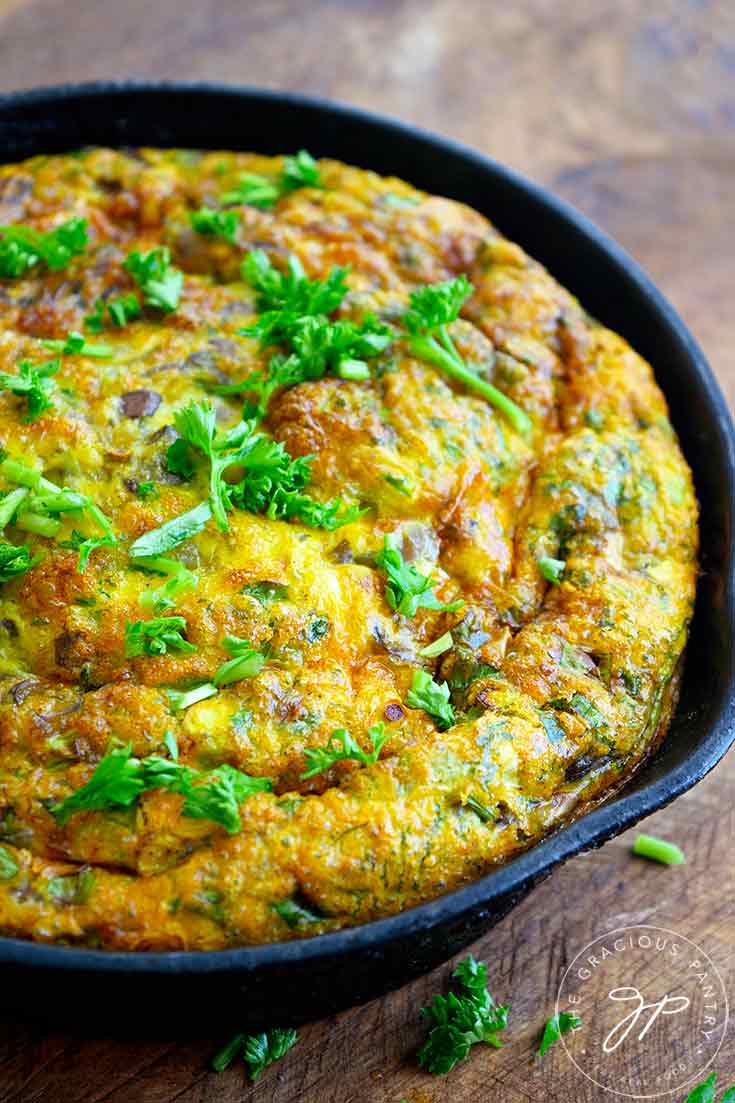 A freshly made frittata sits sprinkled with fresh parsley in a black, cast iron pan in this guide to How To Make A Frittata