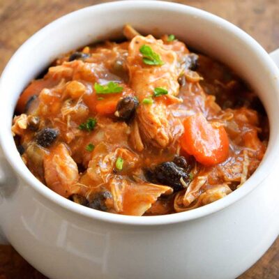 A delicious bowl of this Chicken Stew Recipe sits warm and inviting. You can see bits of black beans and carrots amidst the chicken and red sauce.