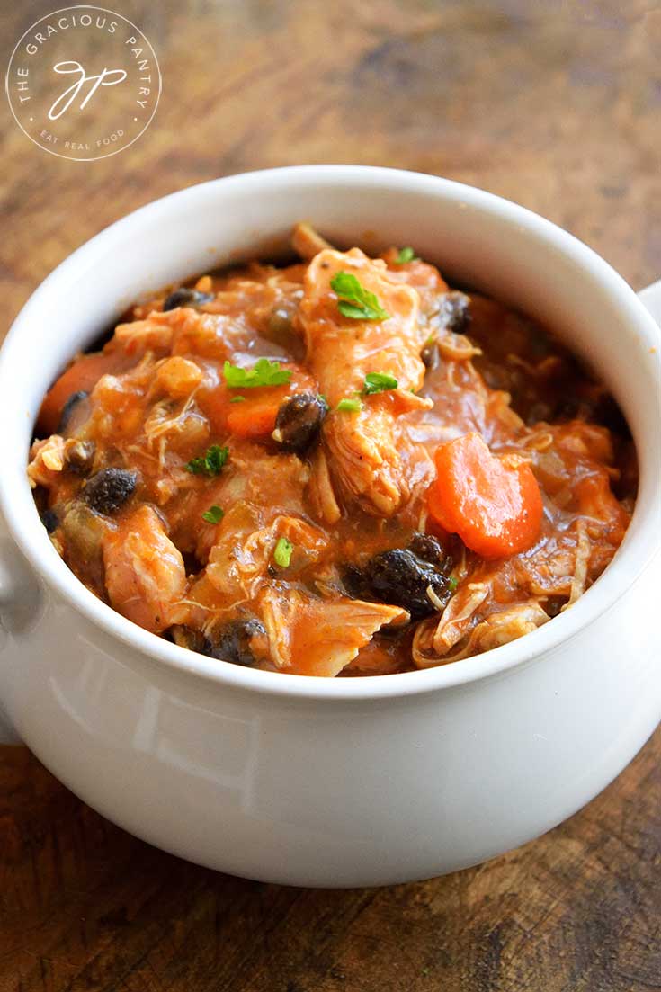 A delicious bowl of this Chicken Stew Recipe sits warm and inviting. You can see bits of black beans and carrots amidst the chicken and red sauce.