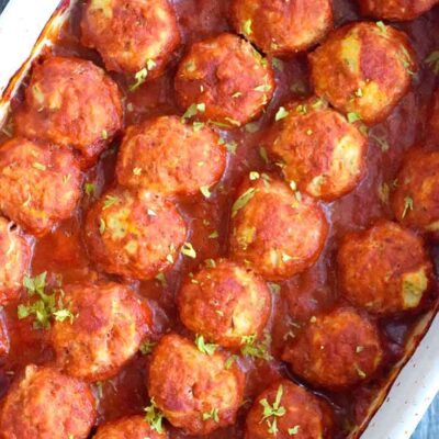 An overhead view looking down into a white casserole dish filled with this freshly made Italian Meatballs.