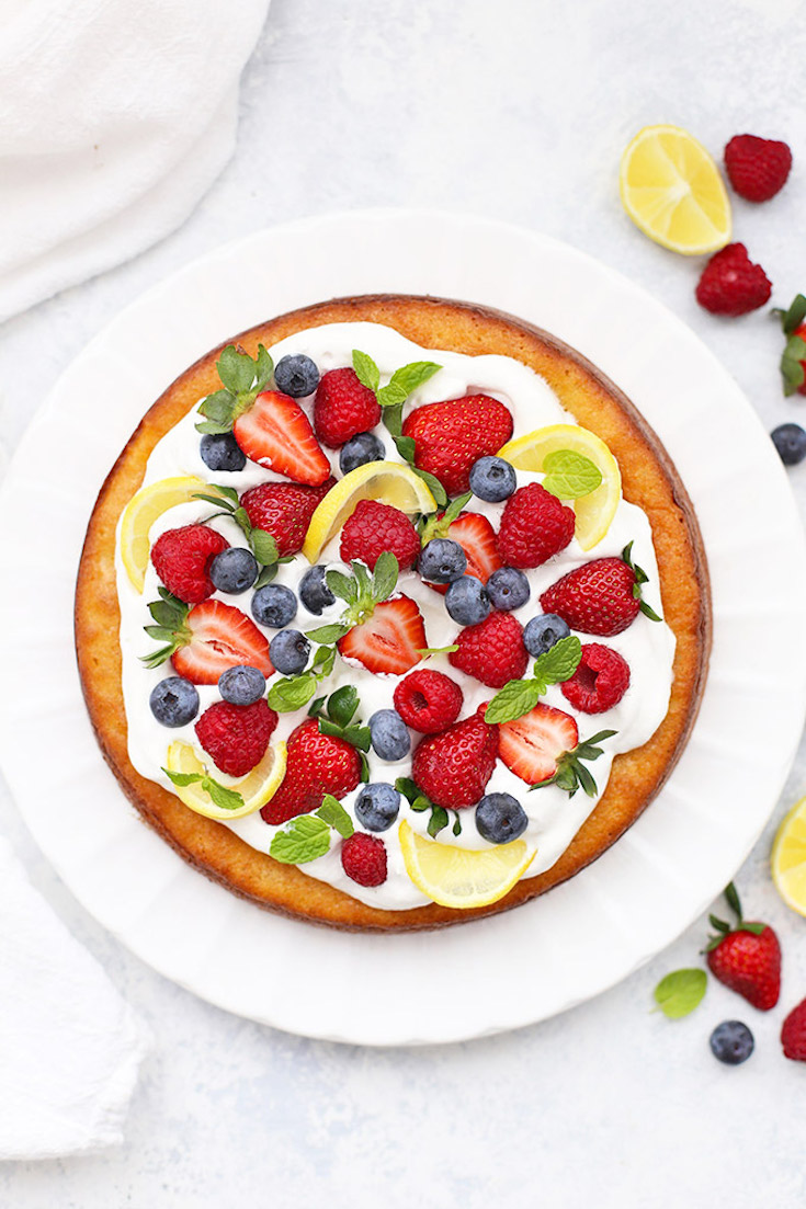 An overhead view of a round lemon cake garnished with strawberries, blueberries and lemon slices.