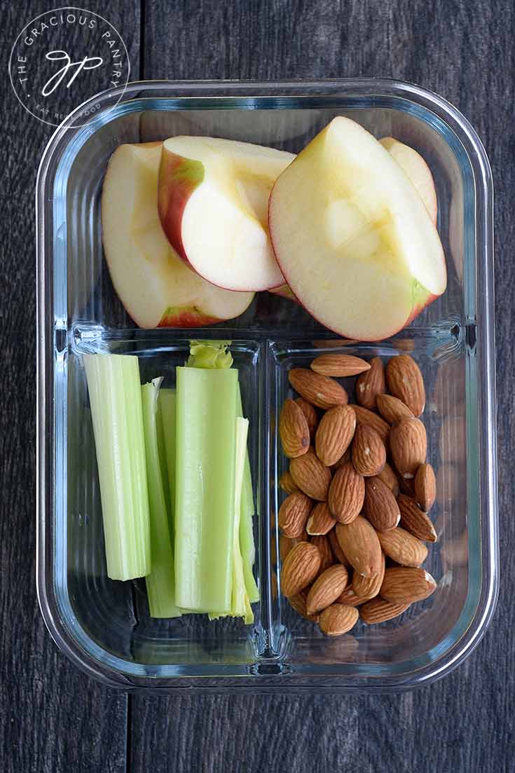 A prep container filled with apples, celery and almonds.