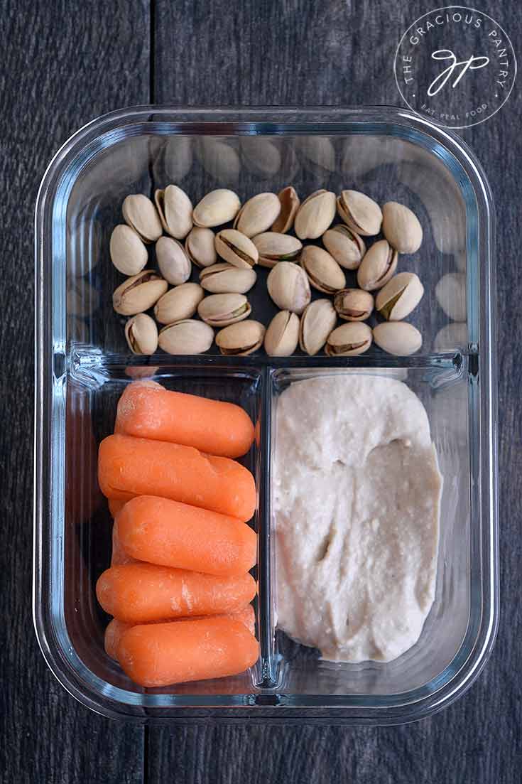 A meal prep container with pistachios, baby carrots and hummus.