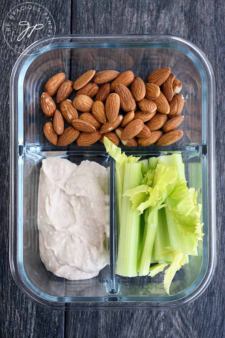 A meal prep container with almonds, celery and hummus.