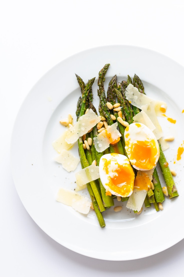 Roasted Asparagus with a cut, soft boiled Egg and Parmesan on a white plate.