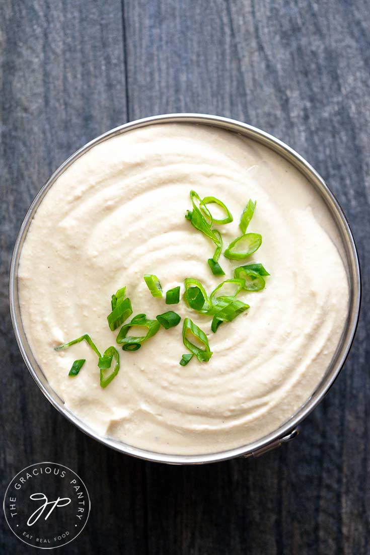 An overhead view of a metal bowl filled with this White Bean Hummus. Sliced green onions garnish the top of the hummus.