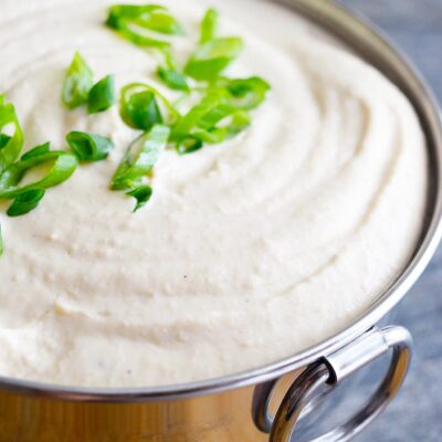White Bean Hummus sits in a metal bowl with sliced green onions for garnish.