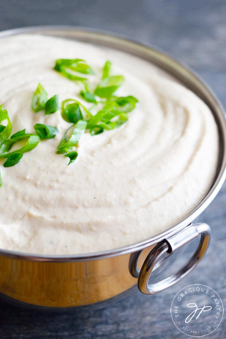 White Bean Hummus sits in a metal bowl with sliced green onions for garnish.